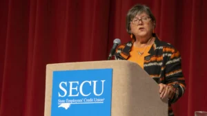 Former SECU Board Member Jo Anne Sanford, speaking into a microphone at a podium on stage.
